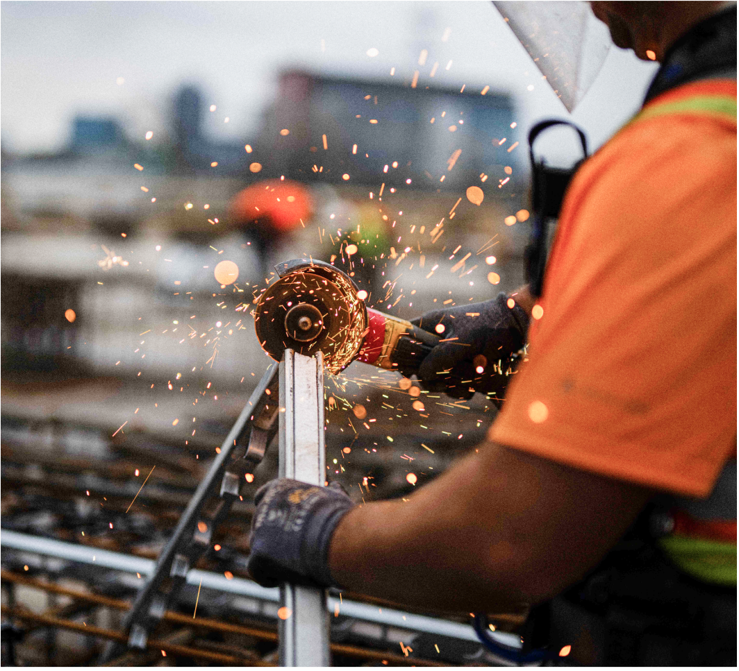 Image of a construction worker using a power cutting tool to cut a piece of metal on a worksite.